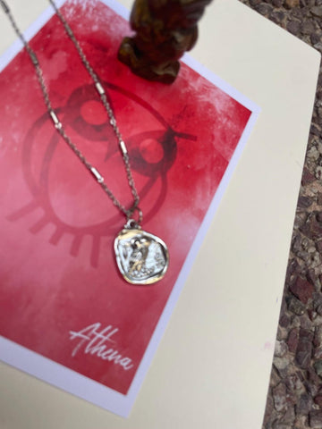 A silver and gold necklace with an owl pendant, displayed on a red background with a note that says 'Athena'.