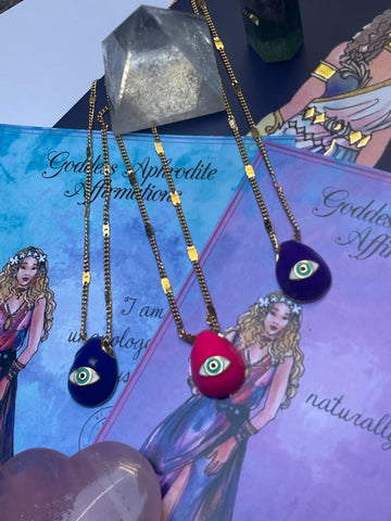 A selection of colorful necklaces with eye designs displayed on a table with a paper featuring illustrations of goddesses.