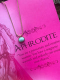 A gold-colored necklace with a teardrop-shaped amazonite pendant, presented on a pink background with text that appears to be a description or quote related to the goddess Aphrodite.