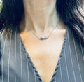 A stainless steel necklace with a winged design, displayed on a tag with an illustration of Hermes, the Greek God of commerce, wealth, and communication.
