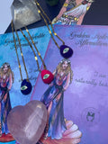 A selection of colorful necklaces with eye designs displayed on a table with a paper featuring illustrations of goddesses.