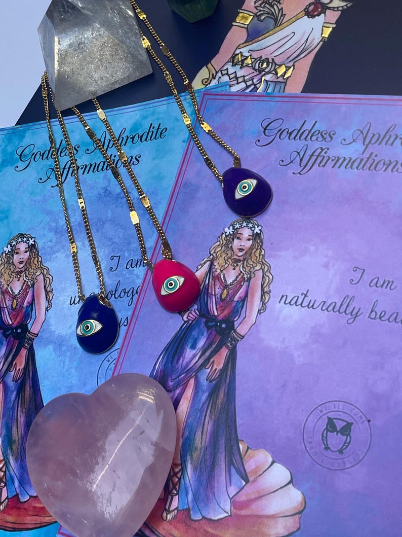 A selection of colorful necklaces with eye designs displayed on a table with a paper featuring illustrations of goddesses.