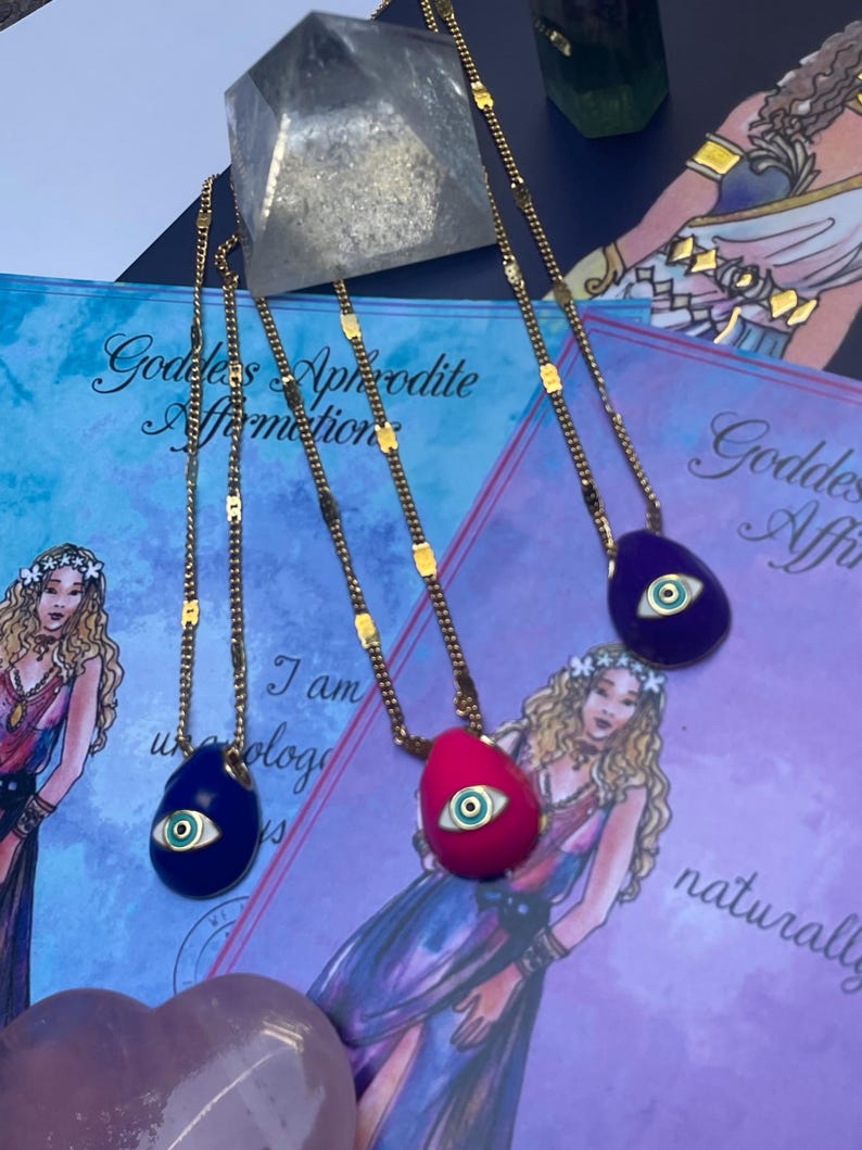 A selection of colorful necklaces with eye designs displayed on a table with a paper featuring illustrations of goddesses.
