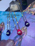 A selection of colorful necklaces with eye designs displayed on a table with a paper featuring illustrations of goddesses.