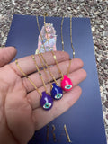 A selection of colorful necklaces with eye designs displayed on a table with a paper featuring illustrations of goddesses.