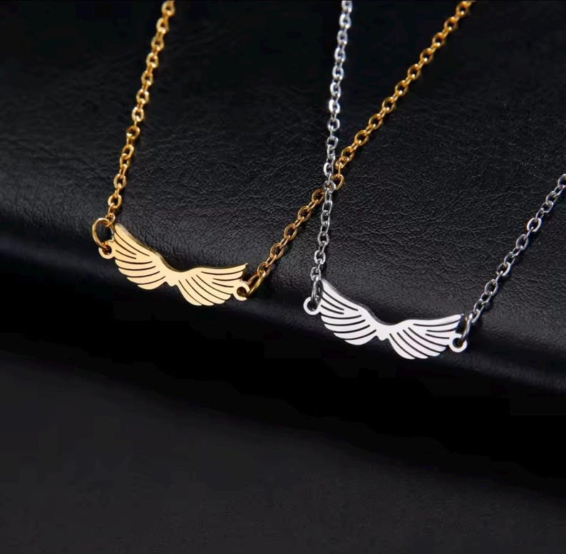 A stainless steel necklace with a winged design, displayed on a tag with an illustration of Hermes, the Greek God of commerce, wealth, and communication.