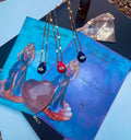 A selection of colorful necklaces with eye designs displayed on a table with a paper featuring illustrations of goddesses.