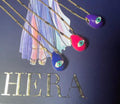 A selection of colorful necklaces with eye designs displayed on a table with a paper featuring illustrations of goddesses.