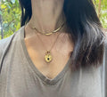 A gold-colored stainless steel necklace with a love symbol pendant, displayed on a card with an illustration of the Greek Goddess of Love, Aphrodite.