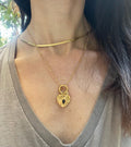 A gold-colored stainless steel necklace with a love symbol pendant, displayed on a card with an illustration of the Greek Goddess of Love, Aphrodite.