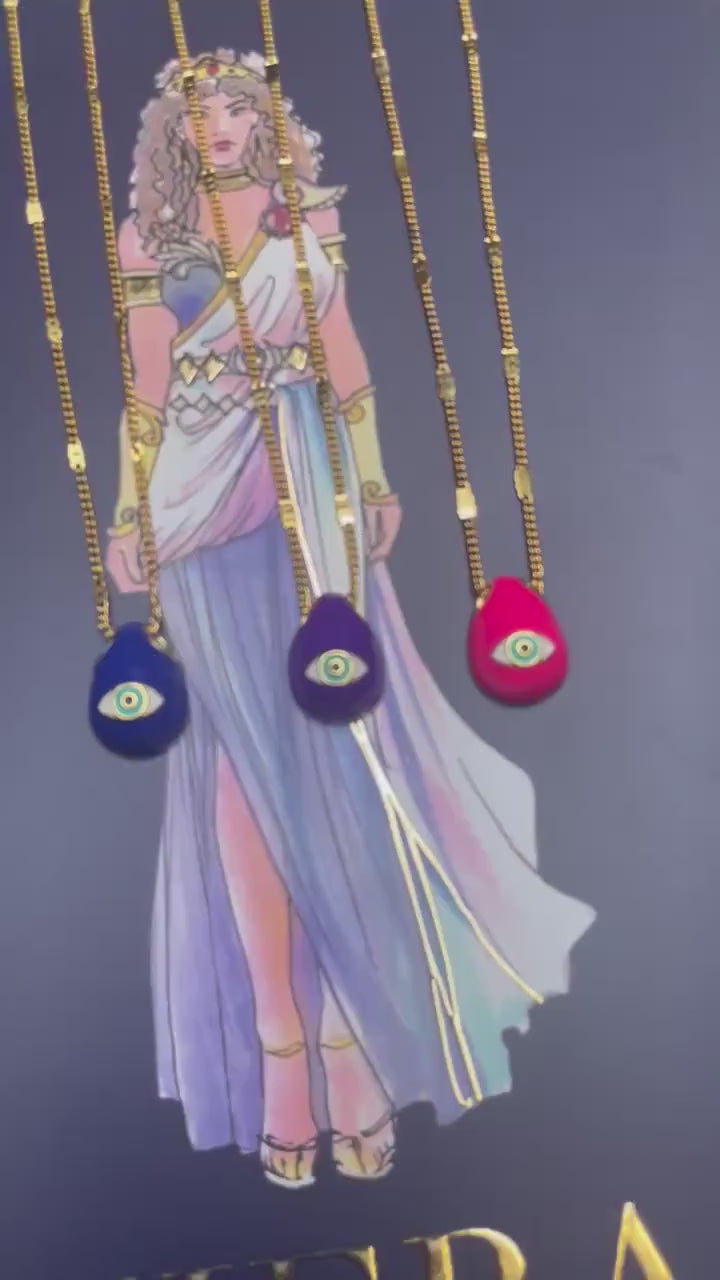 A selection of colorful necklaces with eye designs displayed on a table with a paper featuring illustrations of goddesses.